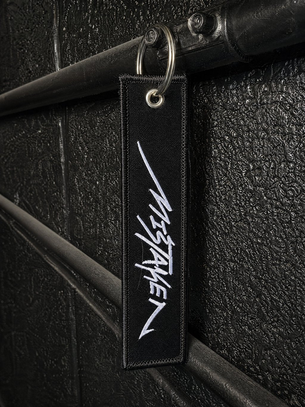 Black keychain with white logo attached to a black textured surface