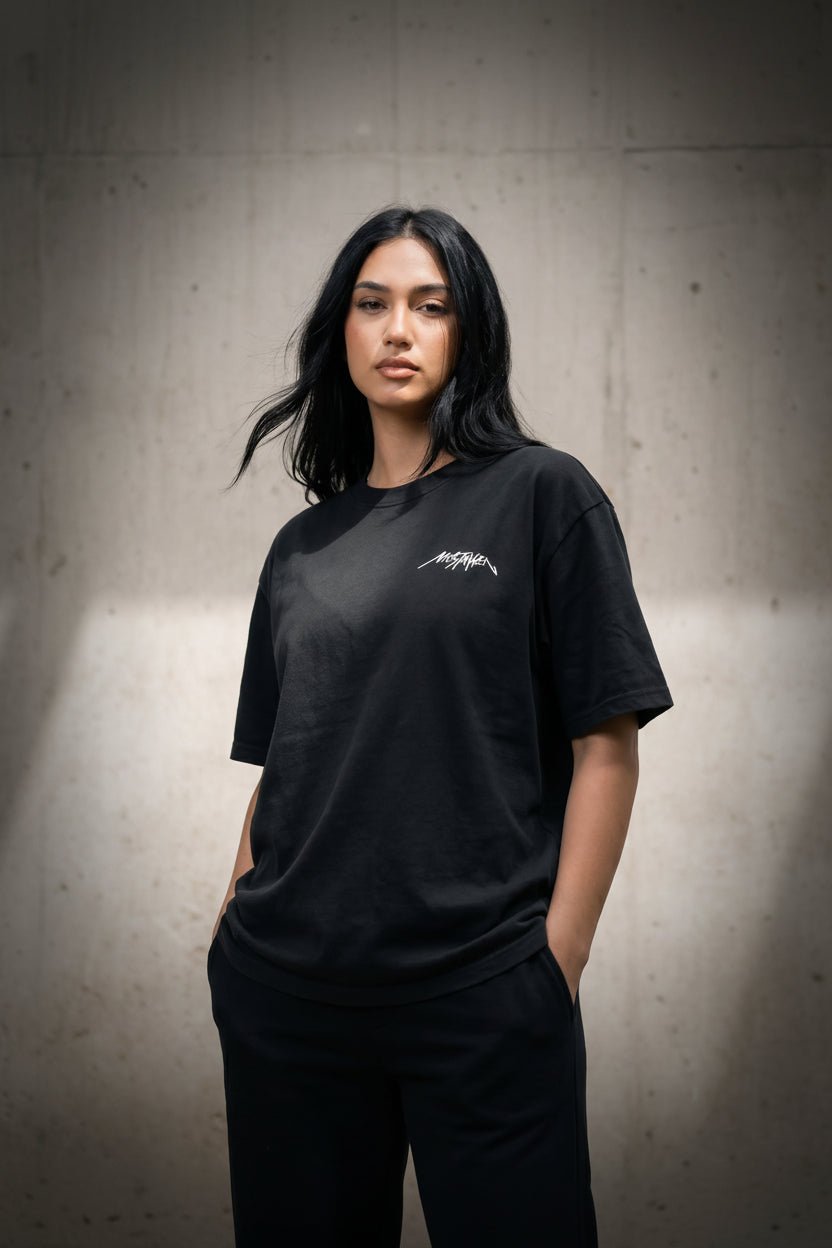 Person wearing a black t-shirt with a logo against a textured wall.
