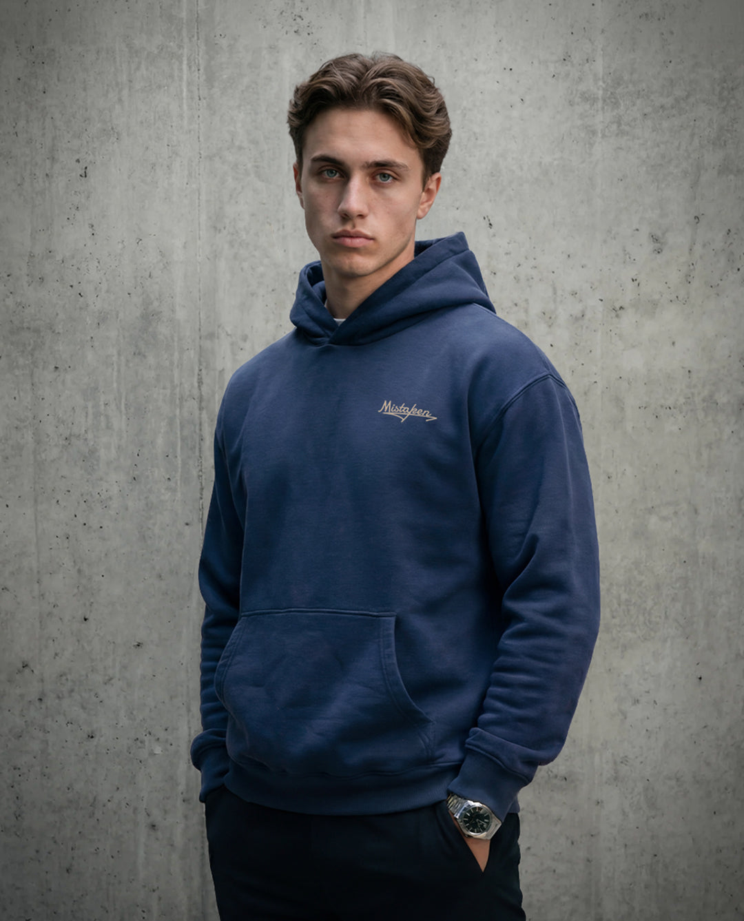 Man wearing a blue hoodie with a logo against a gray concrete wall