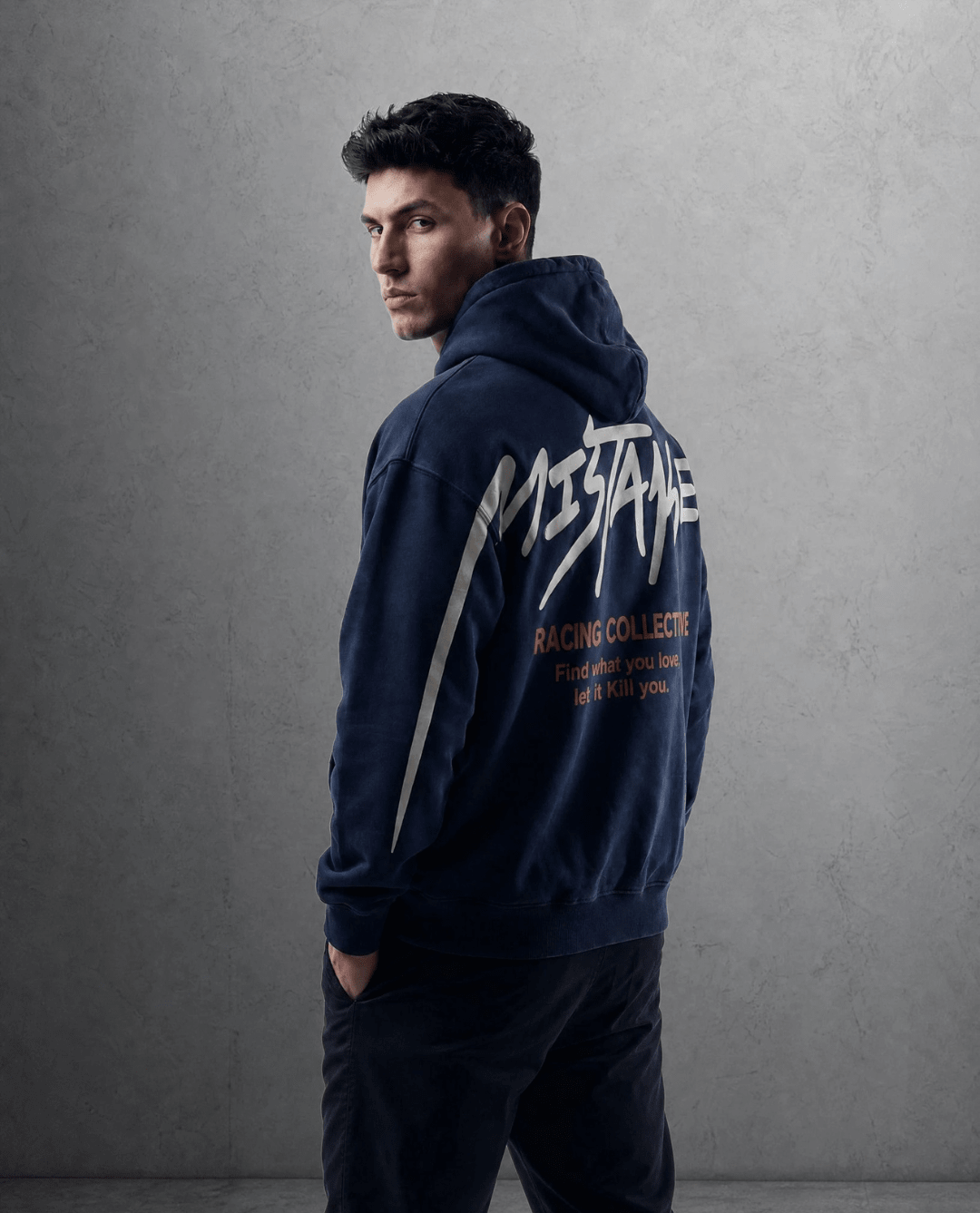 Man wearing a navy hoodie with branding on the back against a gray background
