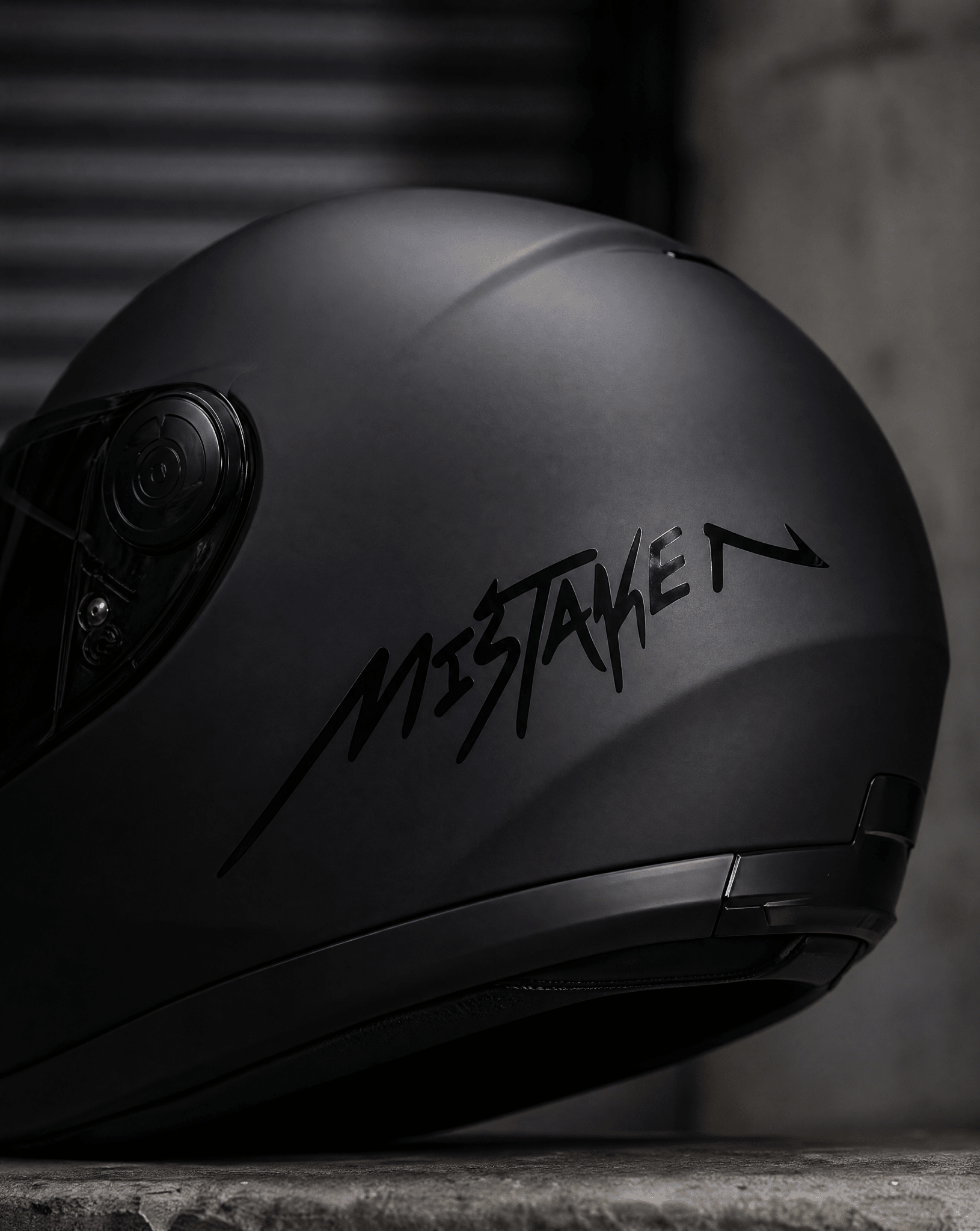Black motorcycle helmet with 'Mistaken' branding on a dark background